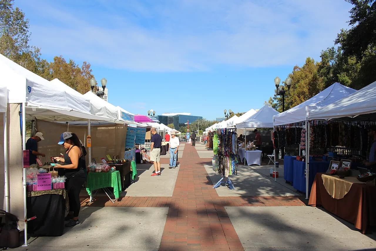 White vendor tents along a path at the Orlando Farmers Market in Lake Eola Park